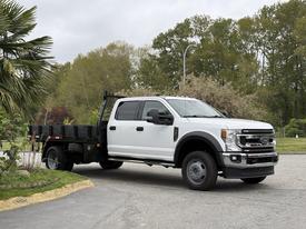 A 2020 Ford F-550 truck with a flatbed and dual rear wheels in a light color positioned at an angle showing its front and side