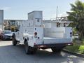 A 2015 Ford F-550 truck with a flatbed and tool compartments in a white finish parked with its tailgate down