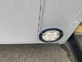 A round LED light fixed to the side of a vehicle with a gray surface near a door hinge