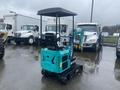 A blue 2024 AGT Industrial MH12R Mini Excavator with a black seat and green arm attachment sitting on tracks in a lot with parked vehicles nearby
