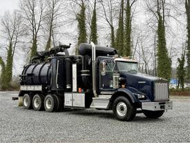A 2018 Kenworth T800 vacuum truck with a black tank and multiple hoses mounted on the chassis, featuring a prominent front grille and side mirrors
