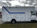 A white 2006 GMC C5000 truck with blue stripes and multiple shuttered compartments along the side