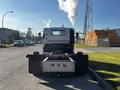 A 2017 Isuzu NQR truck is parked on the street with smoke billowing from its exhaust and a flatbed trailer attached to the rear