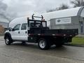 A white 2015 Ford F-550 truck with a black flatbed and tool storage on the back equipped with lights and a protective cage