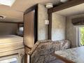 Interior of a 2018 Westland Travelaire showing a textured sofa and mounted refrigerator with a light-colored cabinet above and a table with a patterned surface