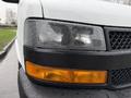 Close-up of the front headlight and turn signal of a white 2021 Chevrolet Express with rain droplets on the surface