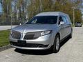 A silver 2013 Lincoln MKT hearse with a sleek design and signature grille features is parked with its headlights on