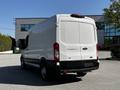 A 2021 Ford Transit van with a white exterior and a high roof is parked, showing its rear doors and large cargo area