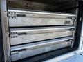 Three metallic storage drawers stacked inside a compartment of a 2004 Freightliner M2 with metal handles for pulling them out