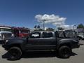 A black 2010 Toyota Tacoma with oversized tires and a custom bed cover is parked in an open area