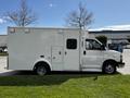 A white 2013 Chevrolet Express van with a boxy design parked on grass with a side view showcasing its large cargo area and single rear wheel on each side