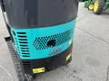 A 2024 AGT Industrial Green QH13R Mini Excavator featuring a black and turquoise body with ventilation slots and safety warning labels