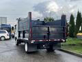 A white 2015 Isuzu NPR HD truck with a black dump body and open tailgate positioned on a paved surface