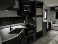 Interior of a 2022 Aspen Trail showing a kitchen area with a sink stove cabinets and appliances including a microwave and refrigerator