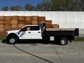 A 2021 Ford F-550 truck with a flatbed design parked on pavement with wooden logs stacked in the background