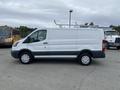 A white 2017 Ford Transit cargo van with metal roof racks and blank sides parked on a concrete surface