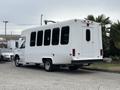 A white 2014 Ford E-350 shuttle bus with large windows and a rear door parked on a concrete surface
