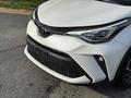 A 2021 Toyota C-HR with a white exterior featuring sharp headlights and a distinctive grille design in the foreground