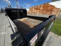 A 2021 Ford F-550 truck with a dump bed in the foreground featuring a metal frame and a partially empty wooden bed