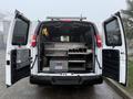 A 2016 GMC Savana van with its rear doors open displaying metal shelving and storage bins inside