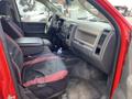 Interior of a 2012 RAM 2500 showing the driver's side seating area with red and black seat covers and a center console filled with items