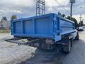 A blue 2009 Dodge Ram 5500 dump truck with a flatbed is parked on the side of the road. The truck's bed is raised, showing a metal frame for transporting materials