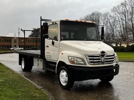 A white 2006 Hino 155 flatbed truck with a black railing on the bed and front grille featuring a circular logo