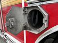 Close-up of an open compartment on a red fire truck with a hexagonal door revealing a round opening inside the compartment