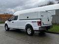 A white 2017 Ford F-150 pickup truck with a truck cap on the bed and 4x4 labeling on the side parked on a wet street