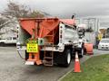 A 2012 International 7400 snowplow truck with an orange plow attached to the front and a salt spreader in the back featuring a caution sign to stay back 15 meters