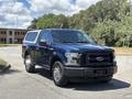 A blue 2015 Ford F-150 pickup truck is positioned in the foreground with a black grille and chrome wheels