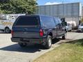 A dark blue 2014 Ford F-250 Super Duty pickup truck with a camper shell in the bed parked on a lot