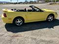 A yellow 2003 Ford Mustang convertible with a black interior parked on a gravel surface featuring a sleek design and chrome wheels