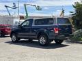 A blue 2015 Ford F-150 truck with silver alloy wheels and a camper shell in the truck bed is parked at an outdoor location