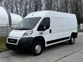 A white 2021 RAM Promaster van with a streamlined design and large cargo area parked at a location with trees in the background