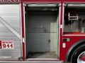 A 1994 Freightliner FL80 fire truck with an empty storage compartment on the side displaying emergency signage and equipment hookup