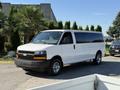 A white 2021 Chevrolet Express van with large windows and chrome wheels parked on a street