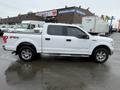 A white 2016 Ford F-150 truck with chrome accents and a four-door cab is parked at an industrial lot