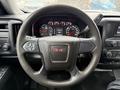 The image shows the steering wheel of a 2015 GMC Sierra 1500 with the GMC logo in the center and various controls on the wheel surface