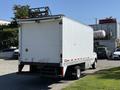 A 2013 Ford Econoline van with a white box truck body and a ladder rack on the roof facing away from the viewer