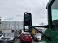 A green 2013 Kenworth T370 truck with a large side mirror reflecting its surroundings and parked cars in the background