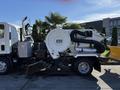 A 2016 Isuzu NPR street sweeper with a large round debris tank and a broom attachment on the front for cleaning streets