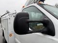 A close-up view of the side mirror of a 2006 Ford F-450 with a rain-covered surface and visibility of a bucket lift attachment on the truck