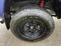 Close-up view of a black alloy wheel and tire from a 2022 Toyota Tacoma featuring an off-road tread pattern and red suspension components in the background