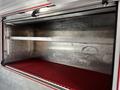 An empty aluminum storage compartment with a red rubberized floor and a metal rail along the top inside a 1994 Freightliner FL80