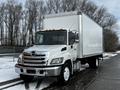 A white 2019 Hino 338 with a 24-foot cube box cargo area parked on a wet surface with trees in the background