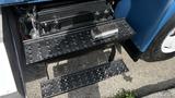 Two black metal steps with perforations leading up to the cab of a 2009 International 4300 truck with a cleaning brush resting on the upper step