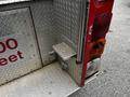 A close-up of a metal step on a fire truck featuring a textured surface and a logo in the center with nearby emergency lights visible