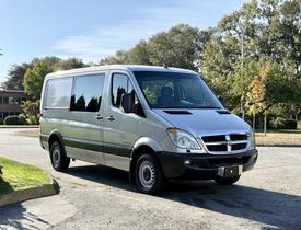 A silver 2007 Dodge Sprinter van with a high roof and large windows parked at an angle