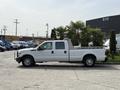 A white 2011 Ford F-350 SD pickup truck with a flatbed and palm trees in the truck bed parked on a concrete surface